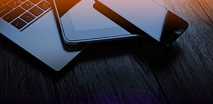Sleek Laptop and Tablet on Dark Wood Desk with Warm Orange Lighting HD wallpaper