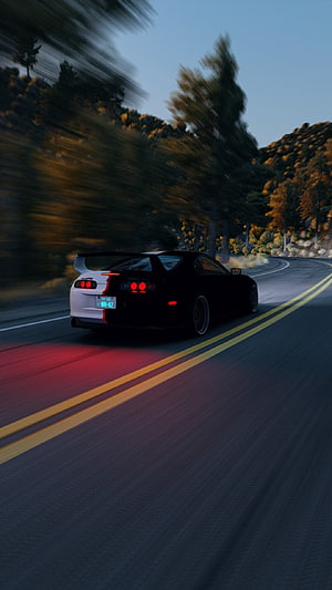 Nissan Skyline GT-R R34 driving on a winding mountain road at dusk with motion blur HD phone wallpaper