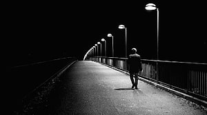 Solitary figure walking along a dark bridge at night under a row of streetlights HD wallpaper