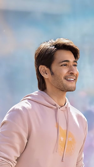 Tiger Shroff smiling in a pink hoodie with a soft blue background HD phone wallpaper