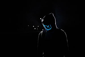Silhouetted figure wearing a glowing neon blue mask in a dark night setting HD wallpaper