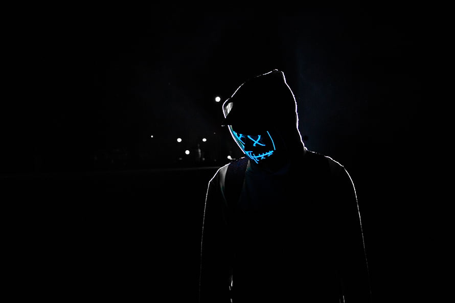 Silhouetted figure wearing a glowing neon blue mask in a dark night setting HD wallpaper