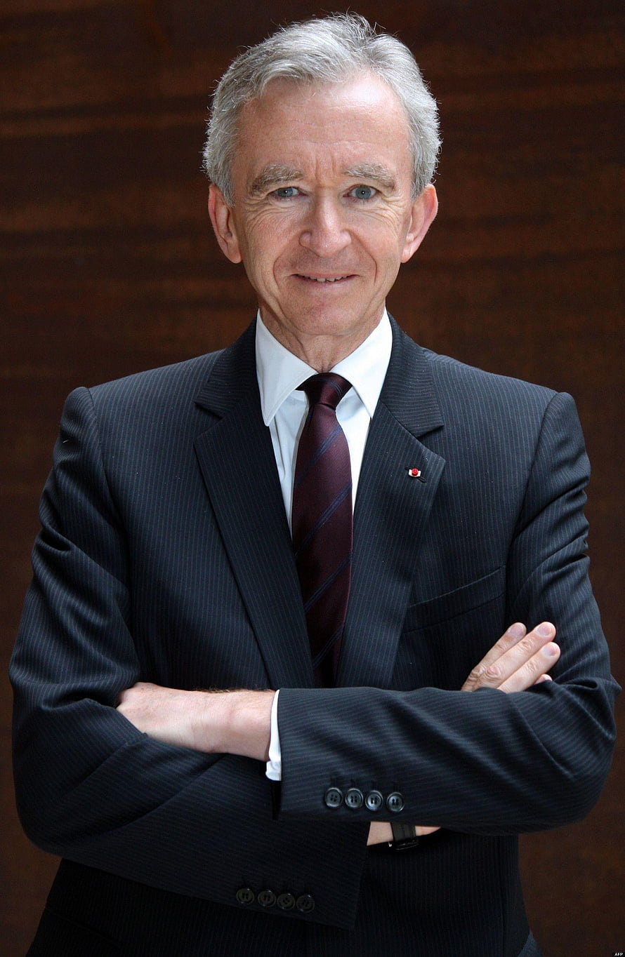 Bernard Arnault in a dark pinstripe suit with arms crossed against a wooden backdrop HD phone wallpaper