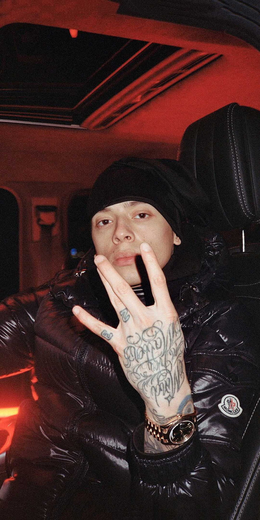 Central Cee in a black puffer jacket with hand tattoos and a gold watch inside a car with red lighting HD phone wallpaper