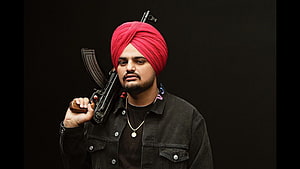 Portrait of a man wearing a red turban and black jacket holding a rifle against a dark background, Sidhu Moose Wala, sidhumooswala HD wallpaper