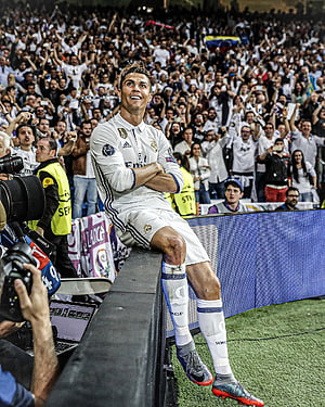 Cristiano Ronaldo sitting on the stadium barrier in Real Madrid kit with fans cheering in the background HD phone wallpaper