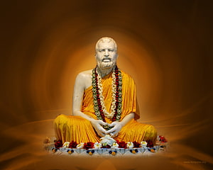 Sri Ramakrishna seated statue in saffron robes with floral garlands and offerings HD wallpaper