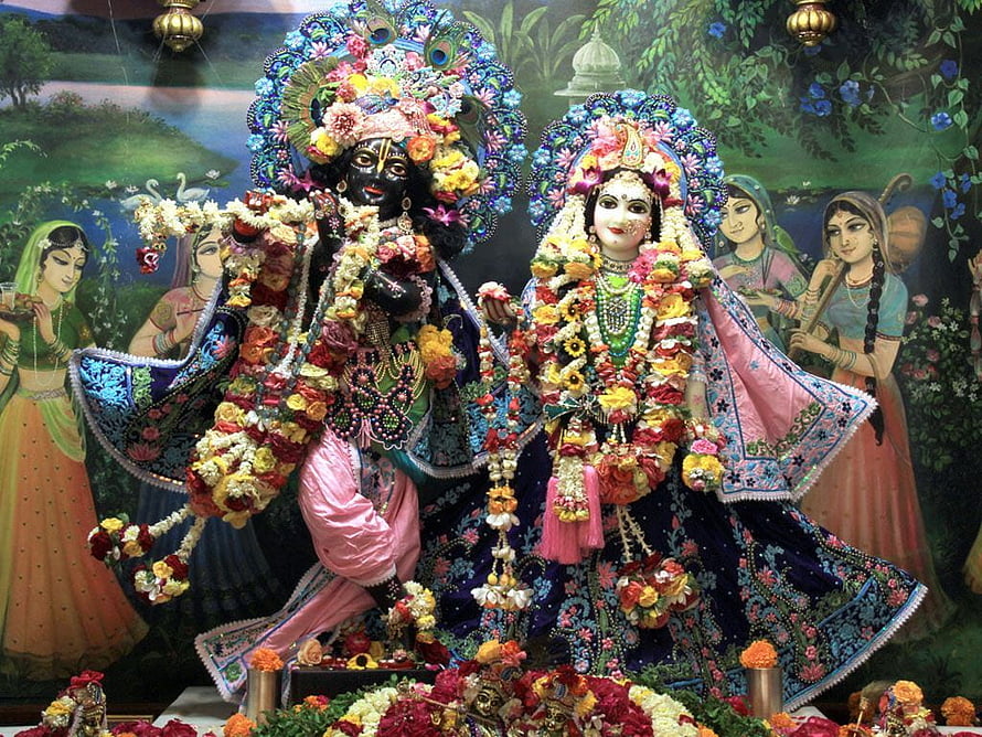 Colorful Radha Krishna idols adorned with flowers and peacock feathers in a festive temple setting HD wallpaper