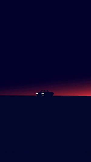 Silhouette of a car with headlights on against a dark blue and red sunset sky HD phone wallpaper