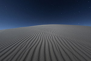 Rippled sand dunes under a star-filled night sky with a deep blue horizon HD wallpaper