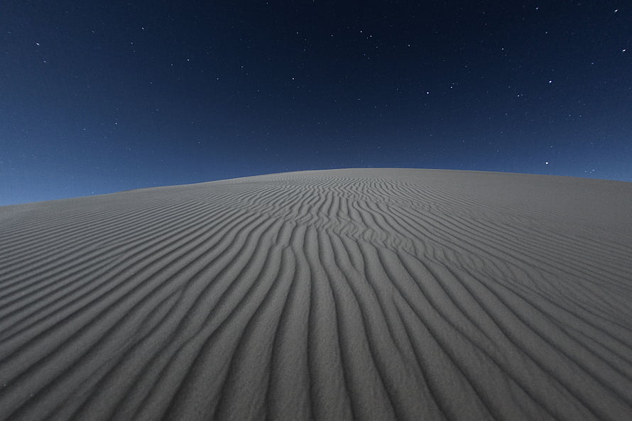 Rippled sand dunes under a star-filled night sky with a deep blue horizon HD wallpaper
