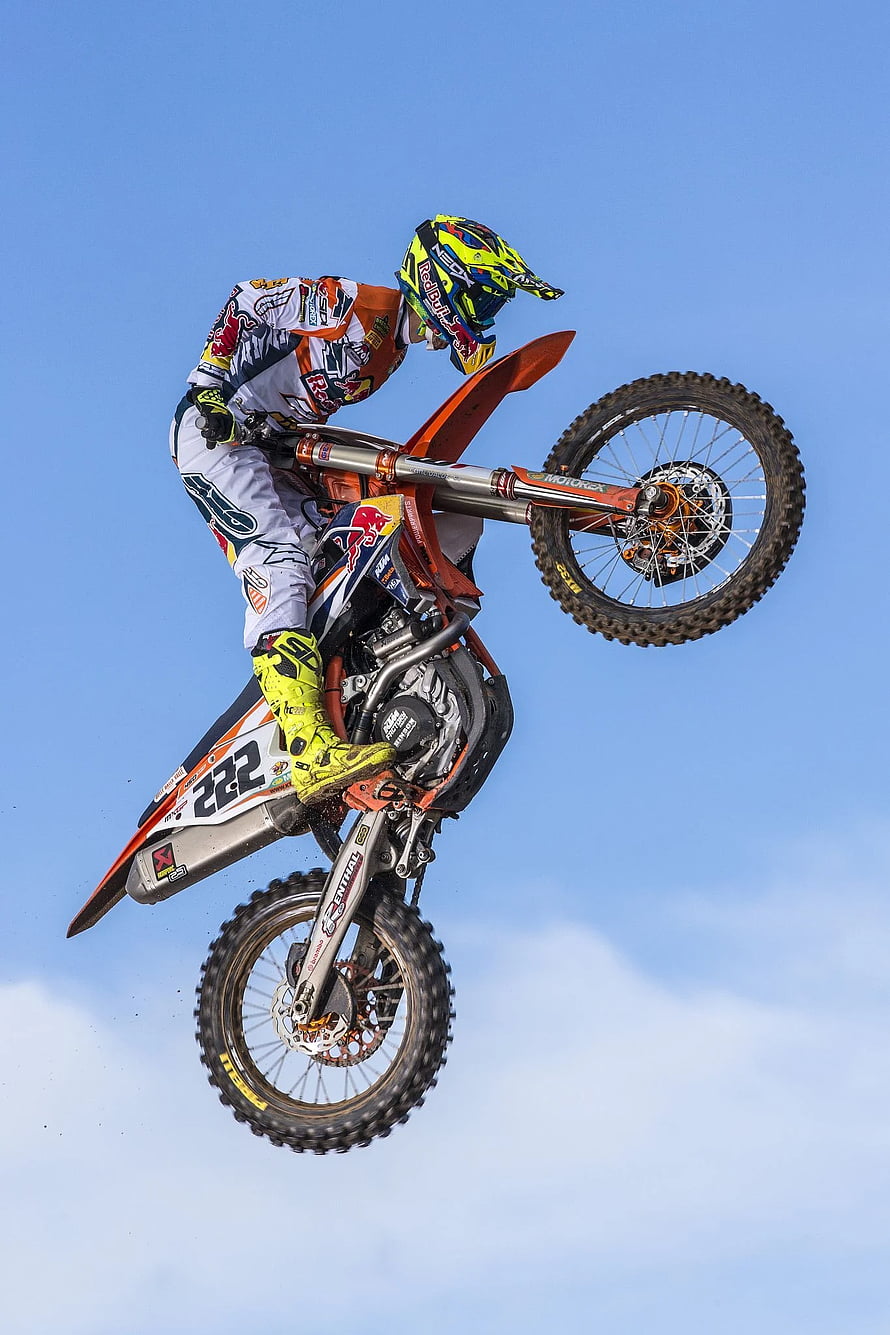 Tony Cairoli mid-air on a KTM dirt bike during a motocross jump against a clear blue sky HD phone wallpaper