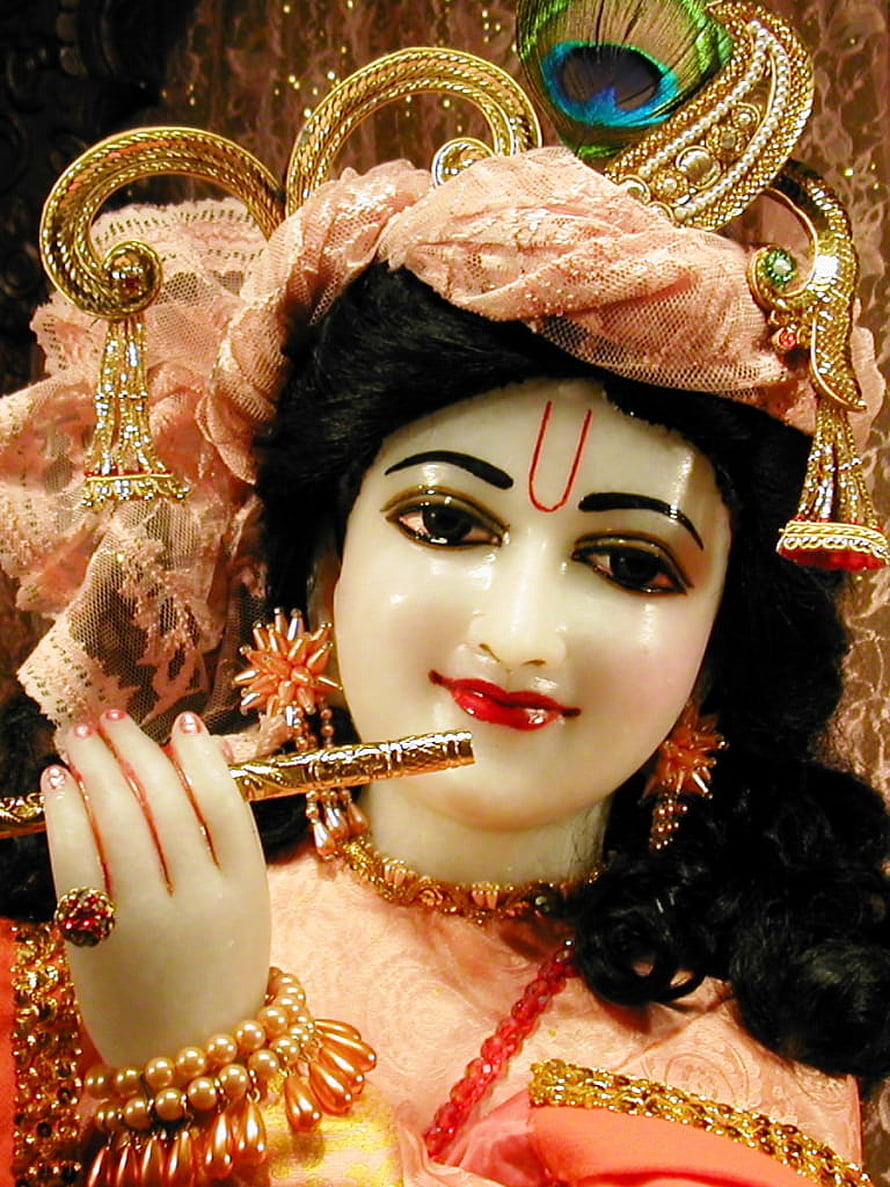 Close-up of a beautifully adorned Krishna idol playing the flute with a peacock feather crown HD phone wallpaper