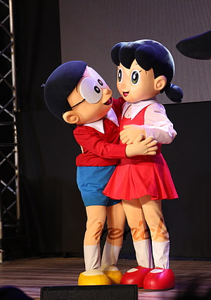Nobita and Shizuka Mascot Costumes Embracing on Stage at Doraemon Event HD phone wallpaper