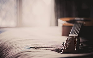 Acoustic Guitar Resting On A Soft Bedspread In A Sunlit Bedroom HD wallpaper