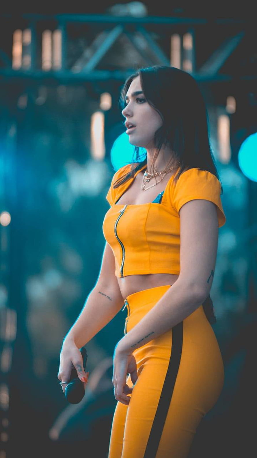 Dua Lipa in a vibrant yellow two-piece stage outfit performing under cool blue concert lighting HD phone wallpaper