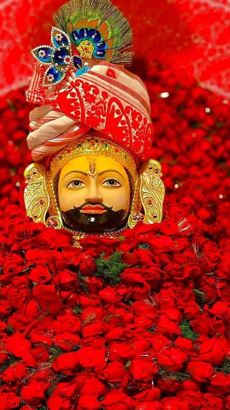 Lord Krishna Statue Adorned With Red Roses And Peacock Feather Crown HD phone wallpaper
