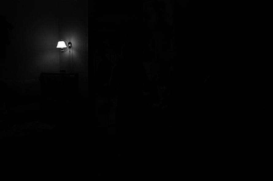 Moody Minimalist Bedroom Scene With Single Wall Sconce Illuminating Dark Interior HD wallpaper
