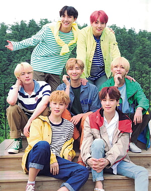 BTS K-pop group members posing together outdoors in colorful casual streetwear on wooden steps HD phone wallpaper