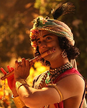 Krishna playing flute with peacock feather crown and traditional jewelry HD phone wallpaper