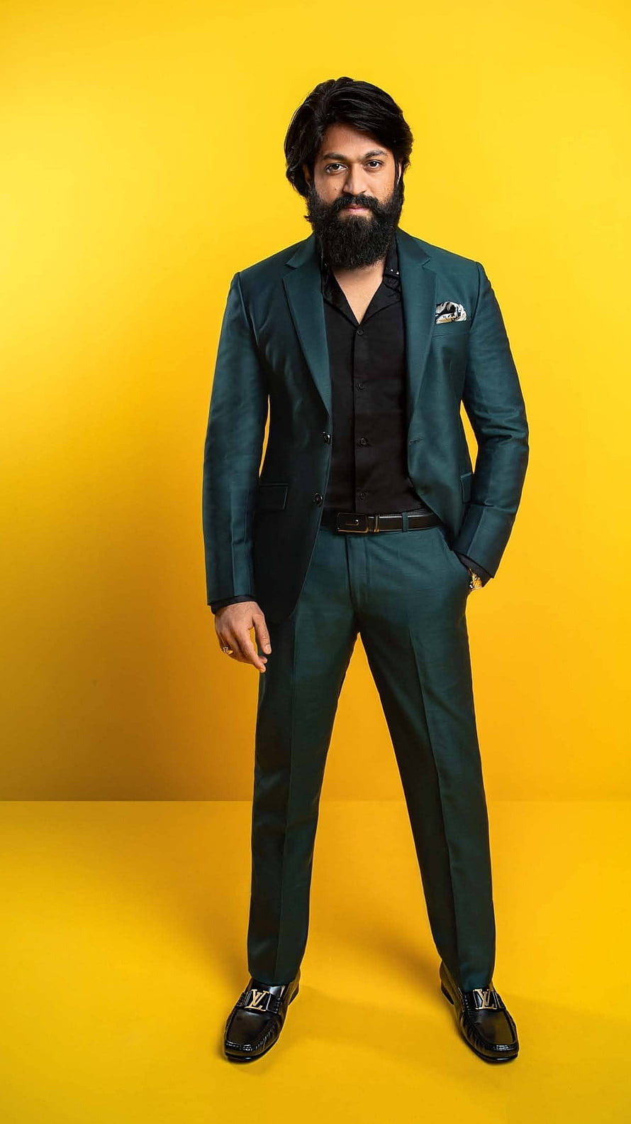 Yash in a dark green suit with black shirt and loafers against a yellow background HD phone wallpaper