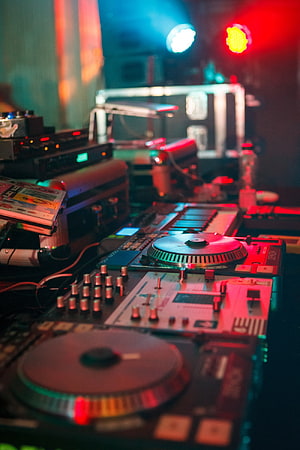 Neon-lit DJ turntables and mixer glowing under red and blue stage lights at a nightclub HD phone wallpaper