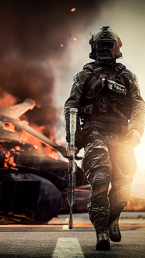 Tactical soldier walking past burning wreckage with rifle in hand HD phone wallpaper