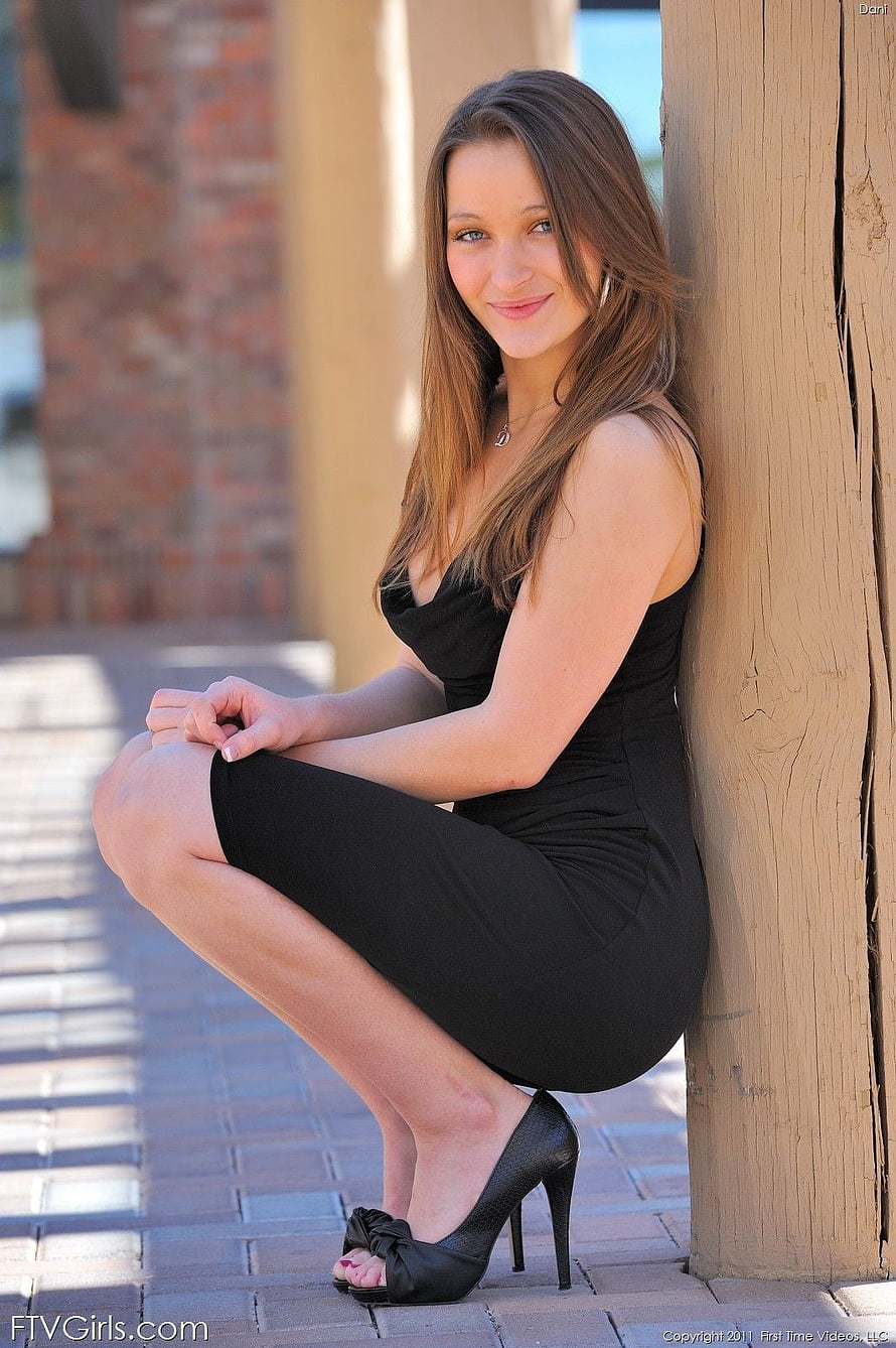 Dani Daniels in a black dress and high heels crouching against a wooden pillar outdoors HD phone wallpaper