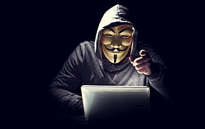 Anonymous Hacker Wearing Guy Fawkes Mask Pointing at Laptop Screen in Dark Room HD wallpaper