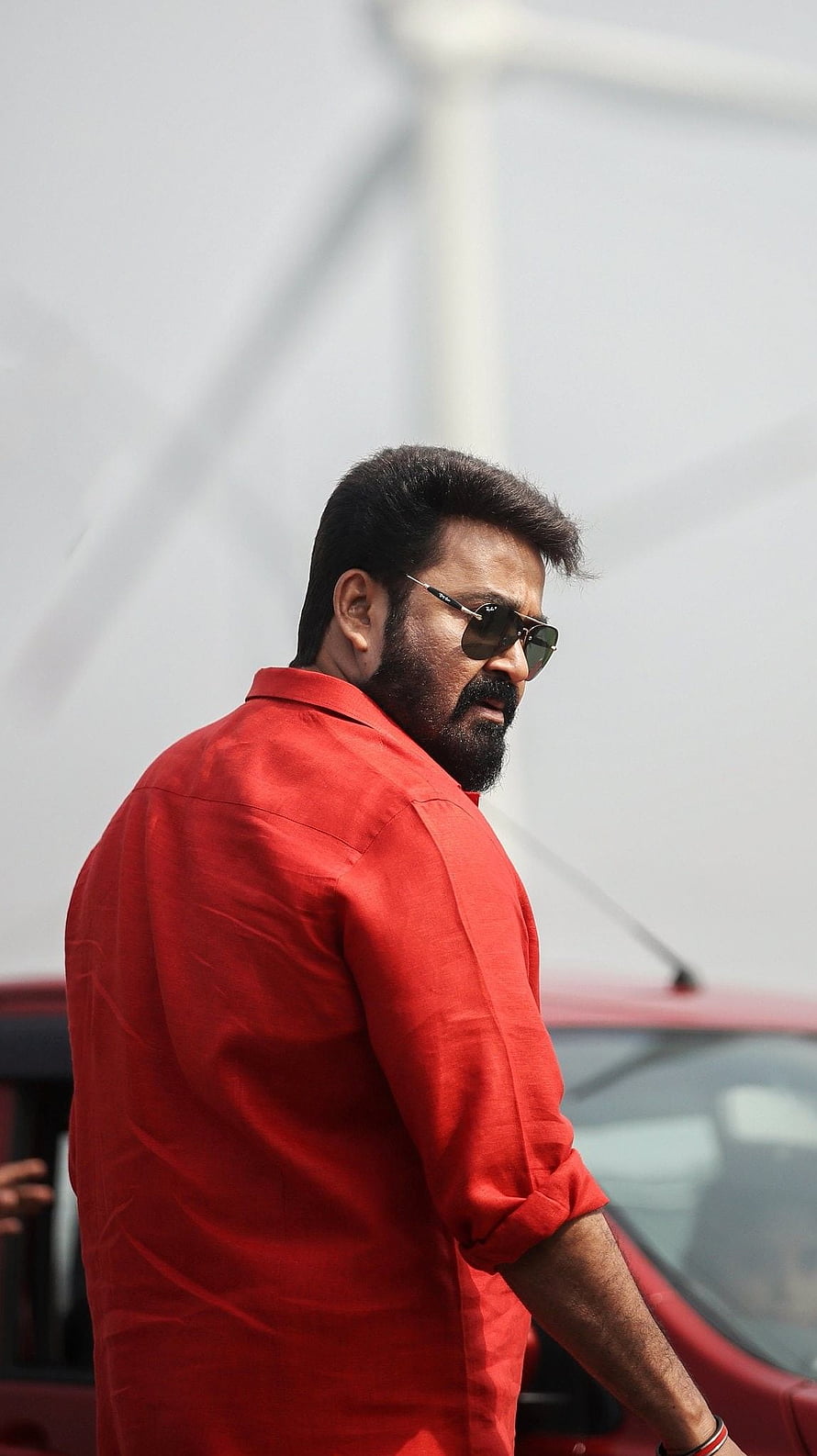 Mohanlal in a red shirt and sunglasses standing beside a car HD phone wallpaper
