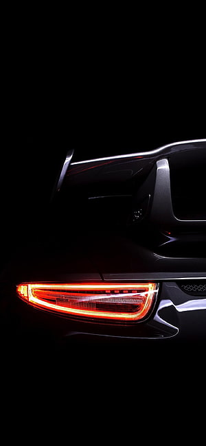Close-up of a sleek black car's glowing red taillight against a dark background HD phone wallpaper