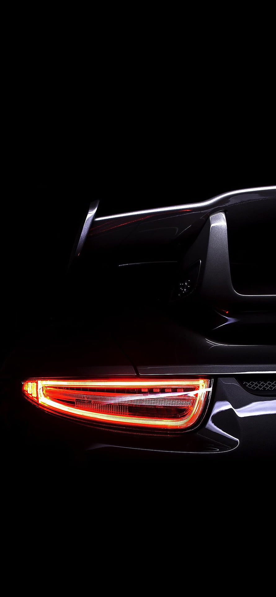 Close-up of a sleek black car's glowing red taillight against a dark background HD phone wallpaper