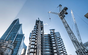 Low-angle view of modern skyscrapers under construction with tower cranes against a clear blue sky HD wallpaper