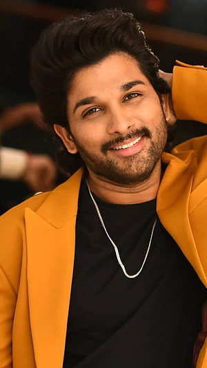 Allu Arjun in a mustard blazer and black tee with a silver chain, smiling with hand behind head HD phone wallpaper