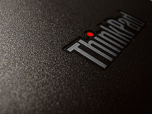 Close-up of the ThinkPad logo on a textured black laptop lid with a red dot accent HD wallpaper