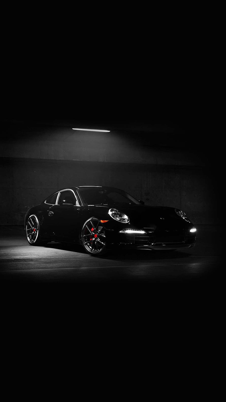 Black Porsche 911 in a dark garage with dramatic overhead lighting and glowing headlights HD phone wallpaper