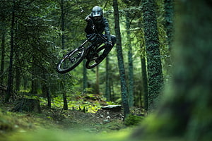 Mountain Biker Jumping Through Dense Green Forest Trail HD wallpaper
