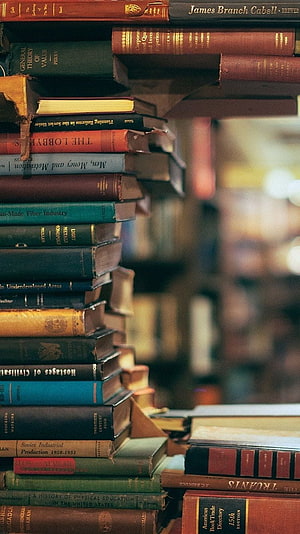 Vintage hardcover books stacked on a library shelf with warm ambient lighting HD phone wallpaper