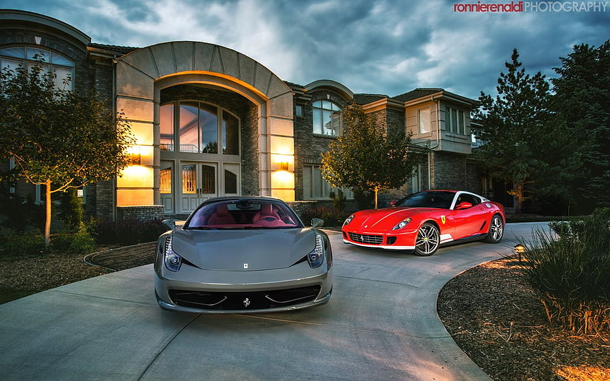 Two Ferrari supercars parked on the driveway of a modern luxury mansion at dusk HD wallpaper
