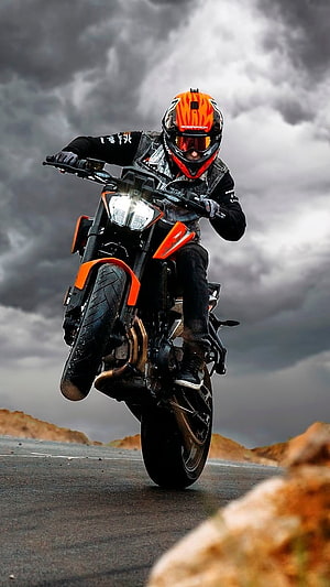 Motorcyclist Performing Wheelie on Orange Bike Under Stormy Sky HD phone wallpaper