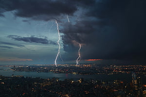 Dramatic Lightning Storm Over a Glowing City Skyline at Dusk HD wallpaper
