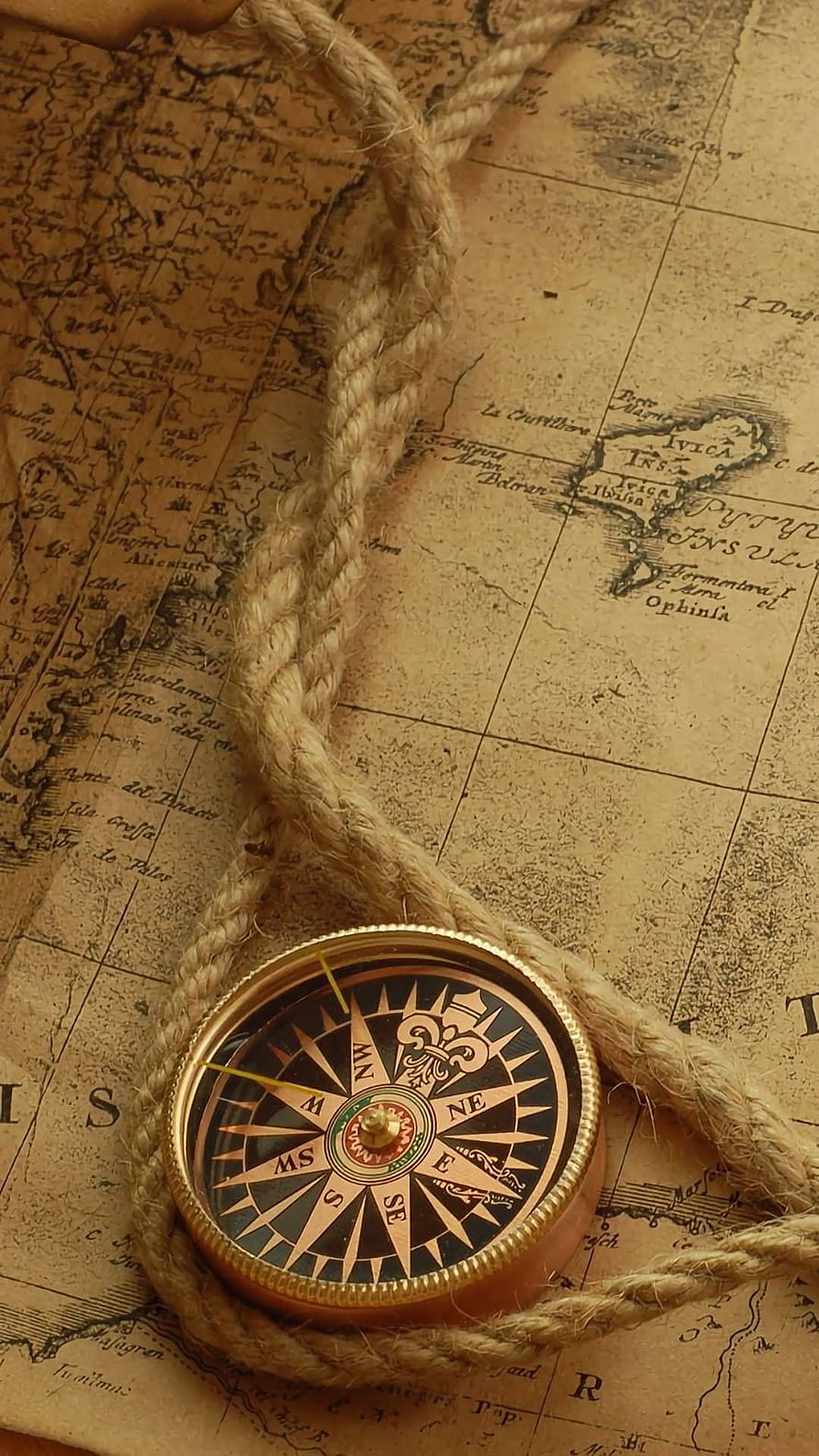 Vintage brass compass resting on an antique nautical map with a coiled rope HD phone wallpaper