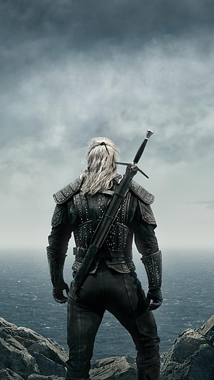The Witcher Geralt of Rivia standing on rocky cliff overlooking misty ocean under stormy sky HD phone wallpaper