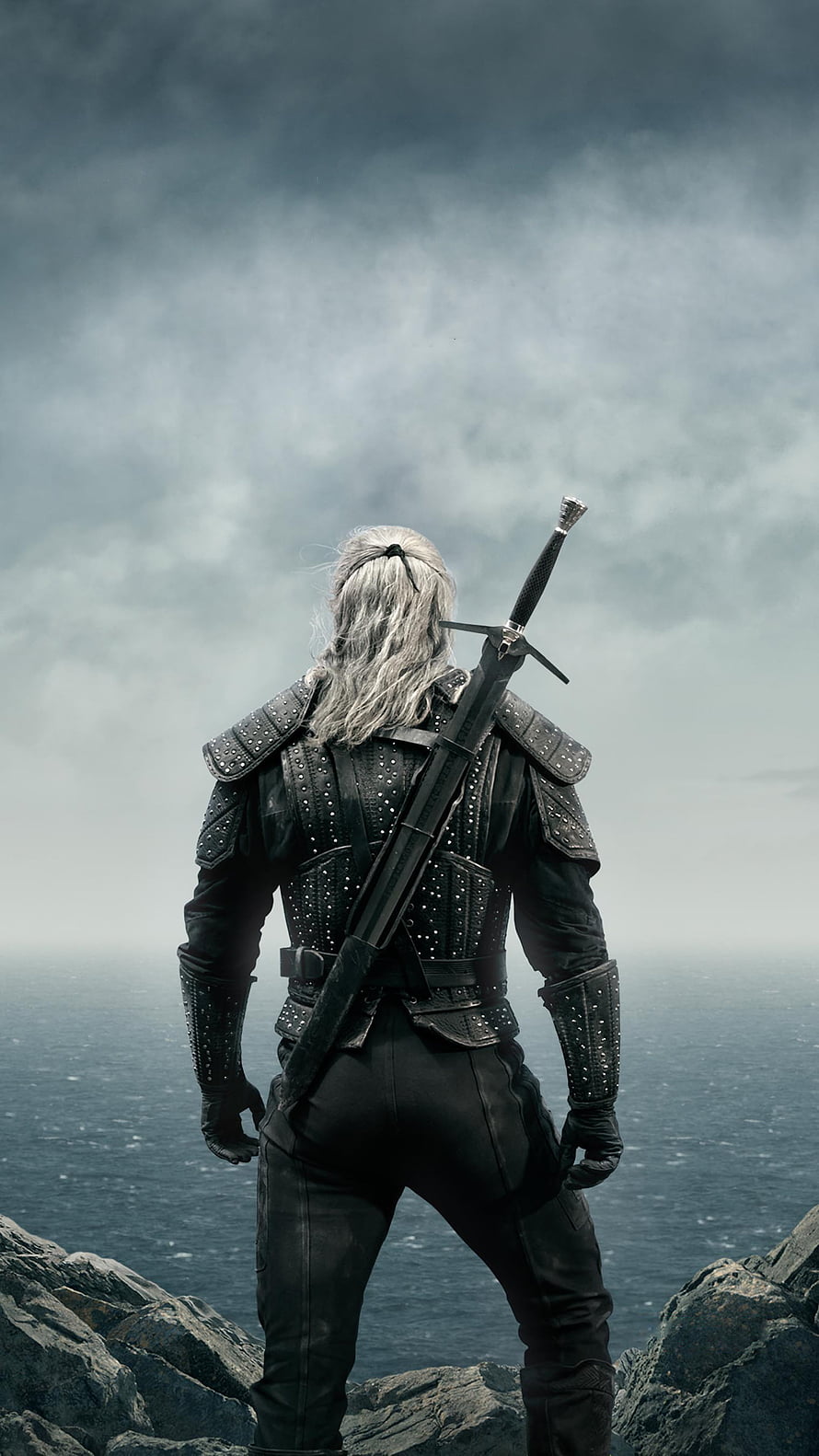 The Witcher Geralt of Rivia standing on rocky cliff overlooking misty ocean under stormy sky HD phone wallpaper