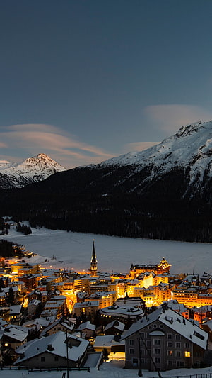 Illuminated Swiss Alpine Town at Dusk with Snow-Covered Mountains and Frozen Lake HD phone wallpaper