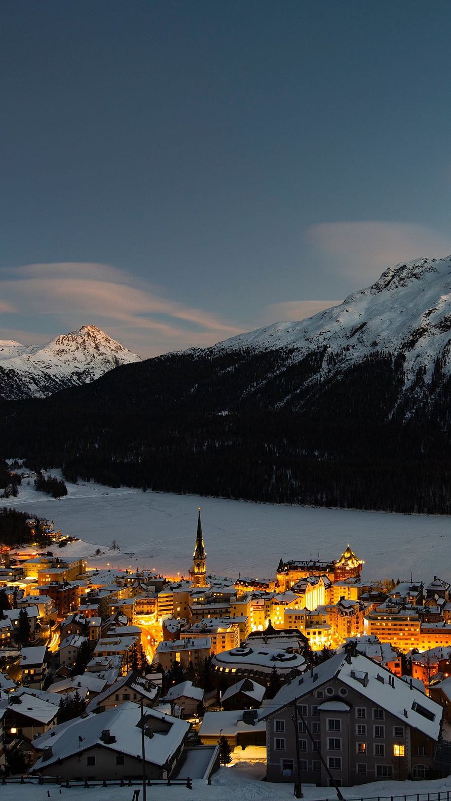 Illuminated Swiss Alpine Town at Dusk with Snow-Covered Mountains and Frozen Lake HD phone wallpaper