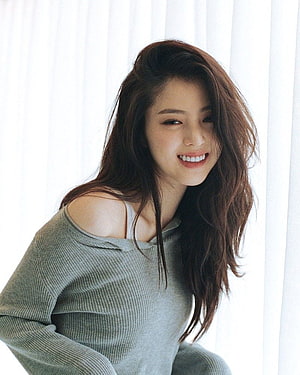 Han So Hee smiling in a grey off-shoulder knit sweater with long wavy hair HD phone wallpaper