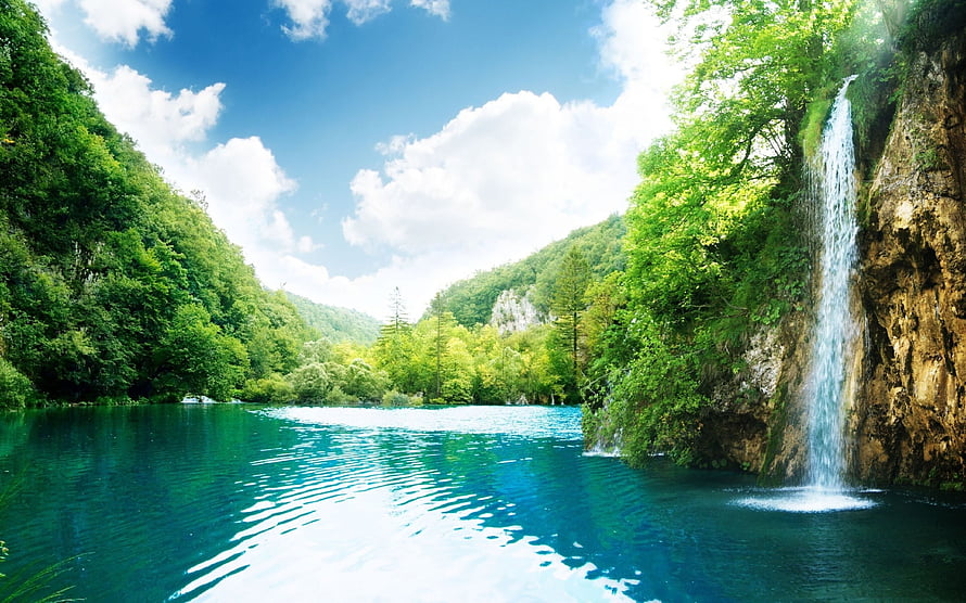 Serene turquoise lake with a cascading waterfall surrounded by lush green forest and blue sky HD wallpaper