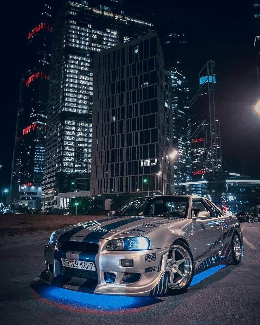 Silver Nissan Skyline R34 GT-R with Blue Stripes and Underglow in City Night HD phone wallpaper