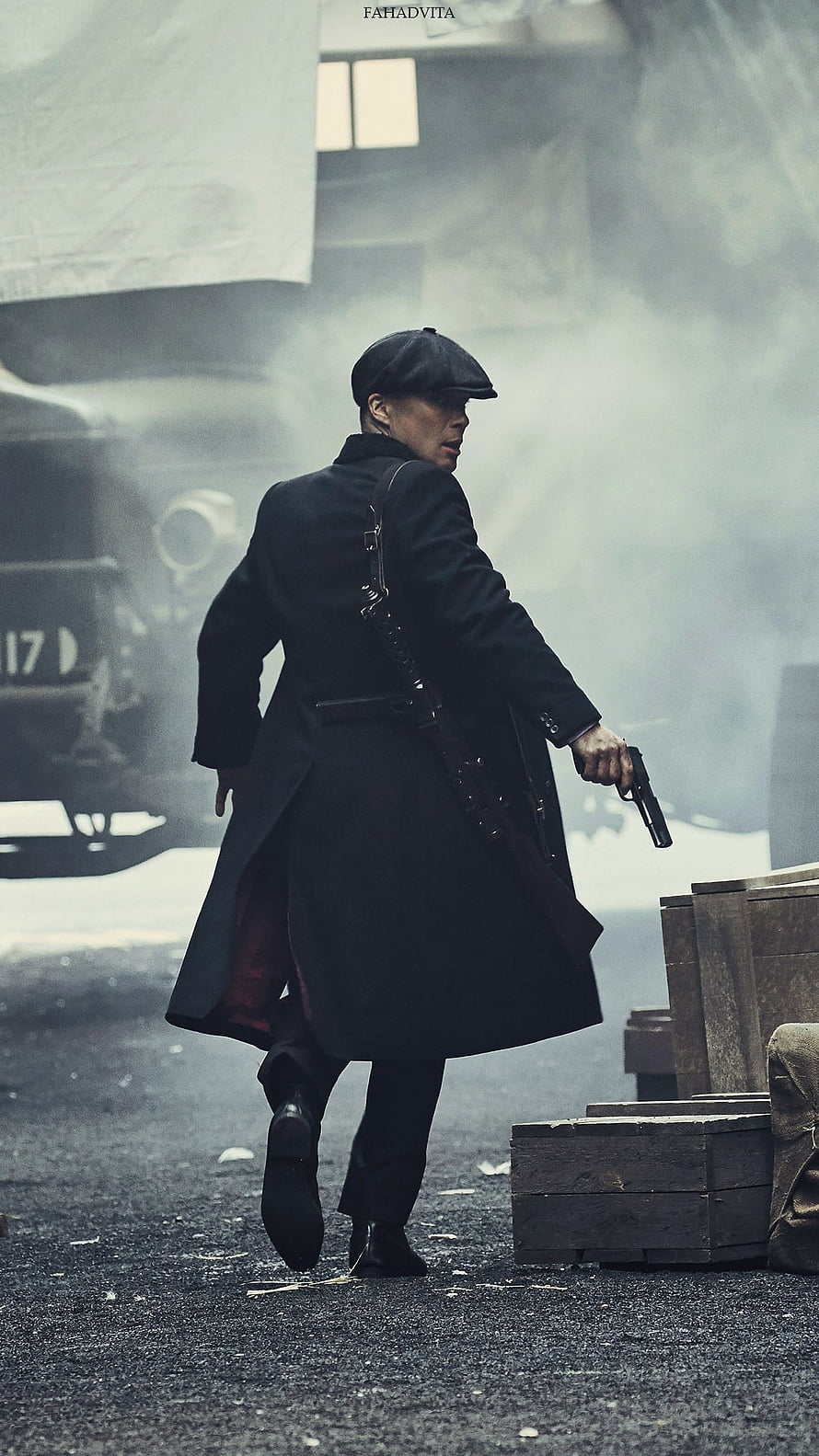 Thomas Shelby from Peaky Blinders in a long black coat and flat cap holding a pistol in a smoky industrial setting HD phone wallpaper